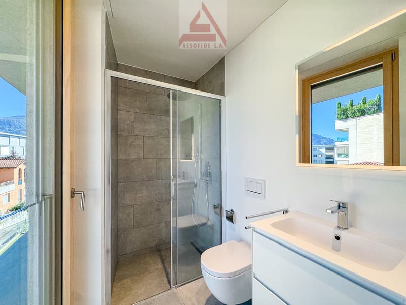 white tiles, glass shower enclosure, white toilet, white sink, wooden framed window