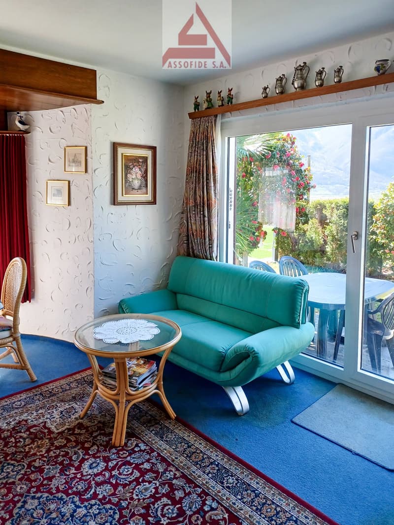 Green sofa, coffee table, rug, chair, glass doors leading to table and chairs in the garden