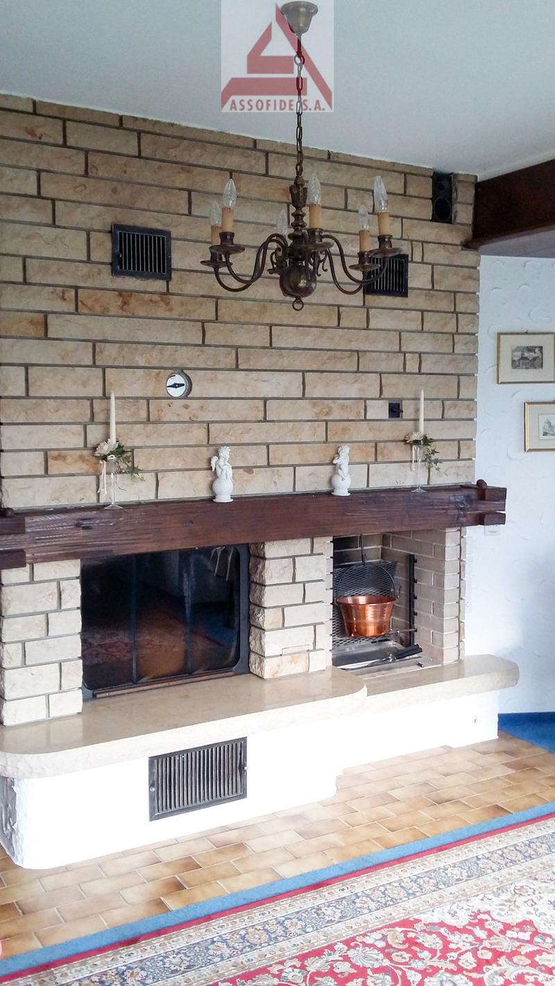 Brick fireplace with a wooden mantel, two candles, a chandelier, a copper pot, and a wooden shelf