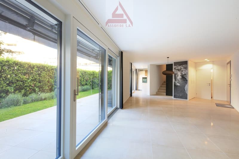 Bright hallway with white tiles, glass doors, large windows, outdoor view of garden, well-lit with natural light