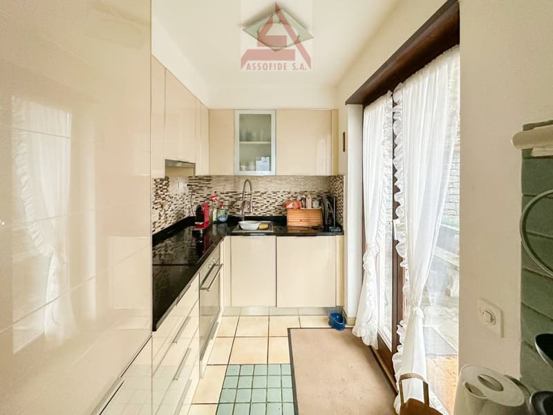 Modern kitchen with white cabinets, black countertops, glass door, sink, faucet, and tiled floor.