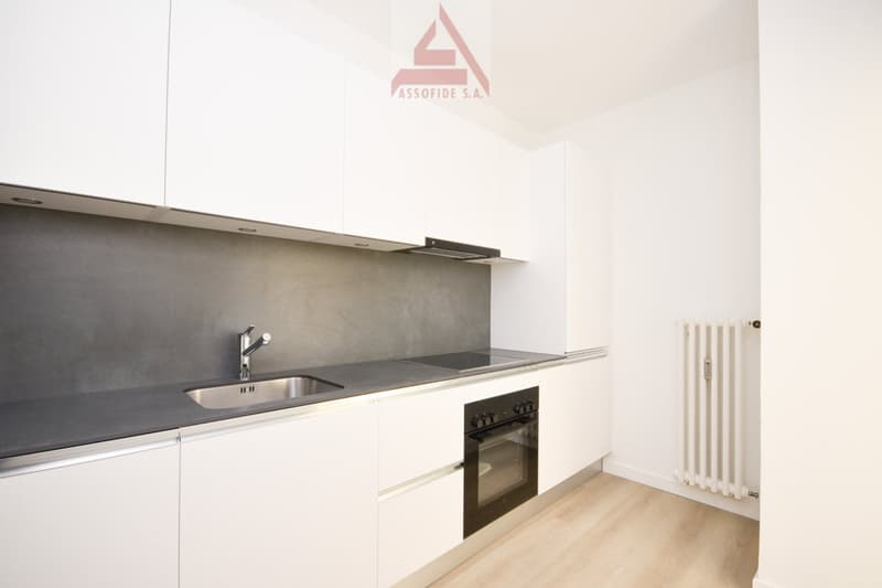 Modern kitchen with white cabinets, granite countertop, integrated dishwasher, and a white washing machine next to the sink.