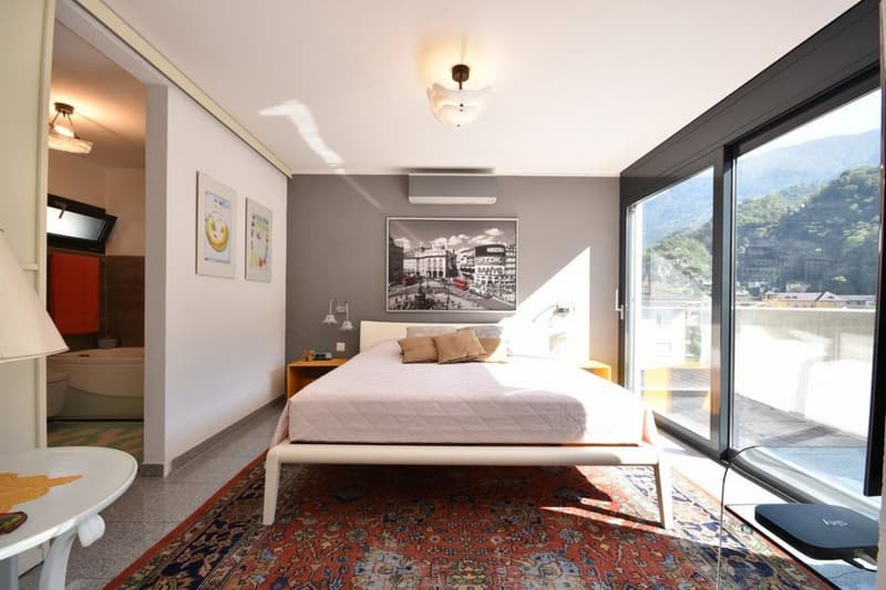 modern decor, gray walls, large bed, large windows, carpet, lamps, paintings, desk, view of mountains