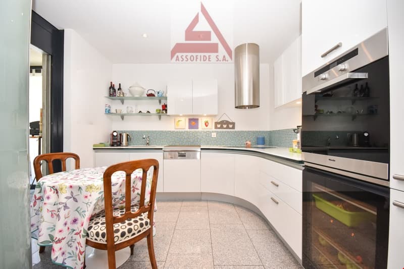 modern kitchen, white cabinets, tile floor, floral tablecloth, dining table, two chairs, dishwasher, two ovens, blue tiled backsplash