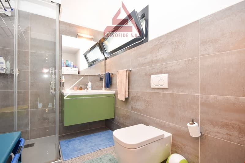modern design, green vanity, white toilet, shower enclosure, beige tiles, blue towels, countertop with toiletries