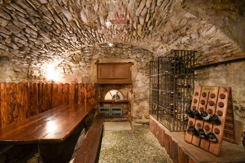 Stone walls, wooden tables, benches, wine racks, metal wine storage, a small arch window