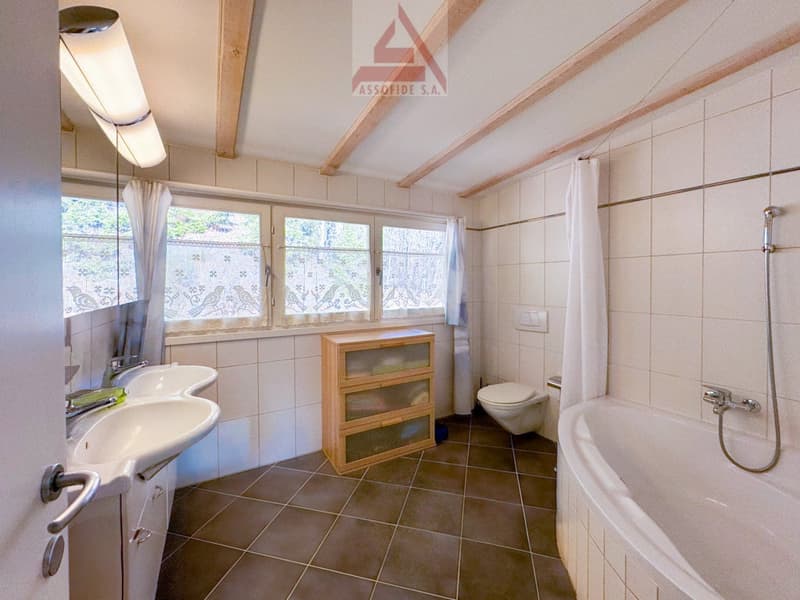Bathroom with bathtub, double sink, toilet, wooden cabinet, white tiles, windows with curtains, and a shower.