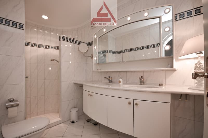 bathroom with white tiles, shower, sink, large mirror, toilet, lamp