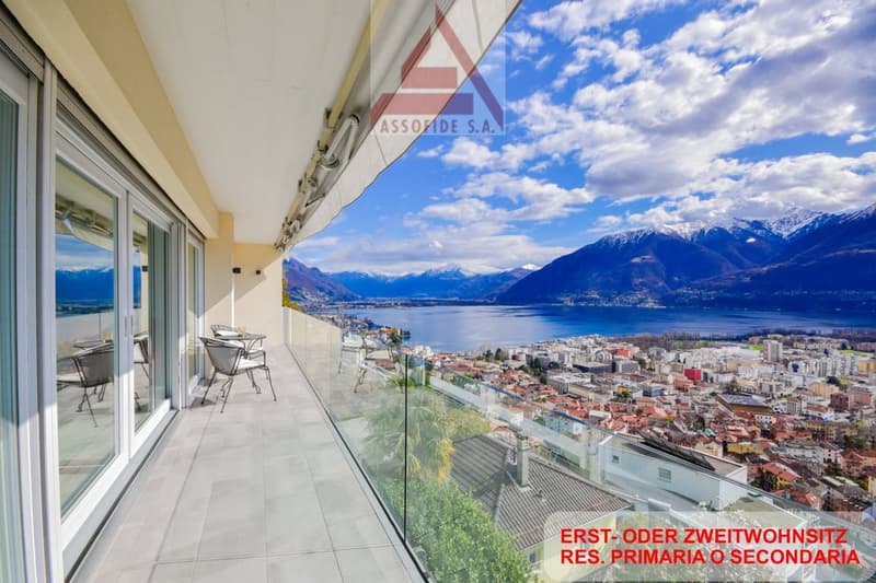 Balcony with glass railing, table and chairs, glass doors, scenic mountain and lake view