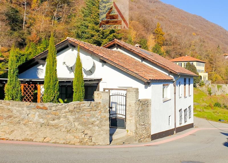 single-storey white house, red roof, chimney, gated entrance, stone fence, mountainous surroundings