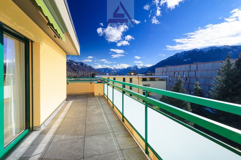 terraced apartment balcony, green railings, clear skies, mountain range in the background