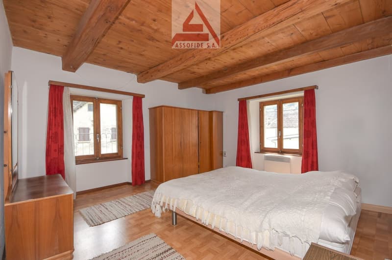 bedroom with wooden bed, wooden wardrobe, wooden floor, two windows with red curtains, white bed sheets, two carpets