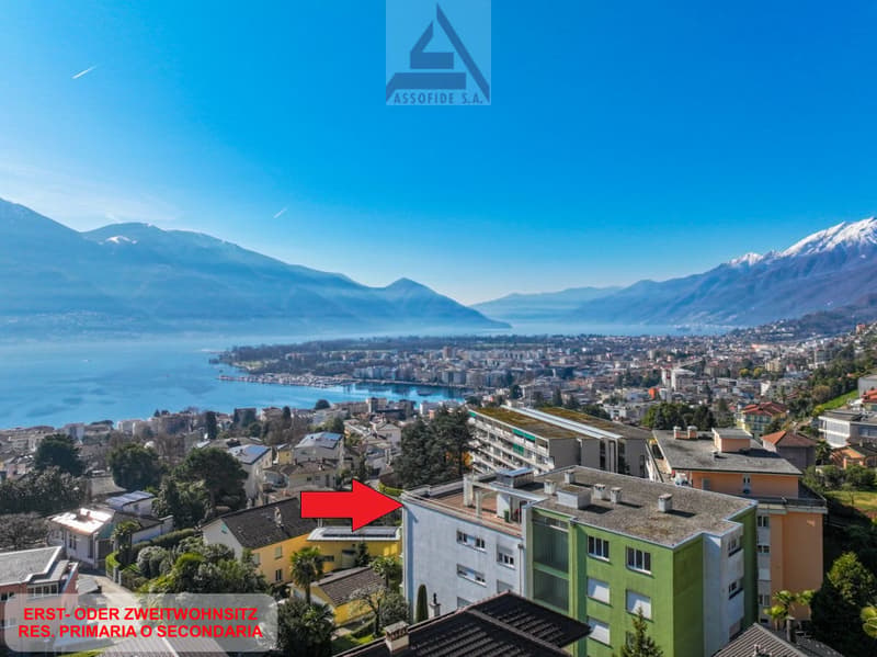 Aerial view of the building with surrounding houses, mountains, and a lake