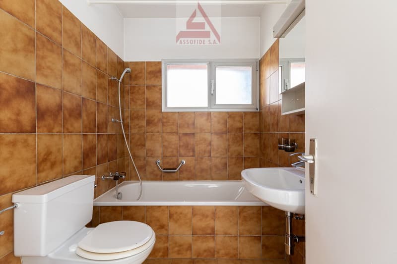 Bathroom with brown tiles, white toilet, bathtub, sink, and shower head.