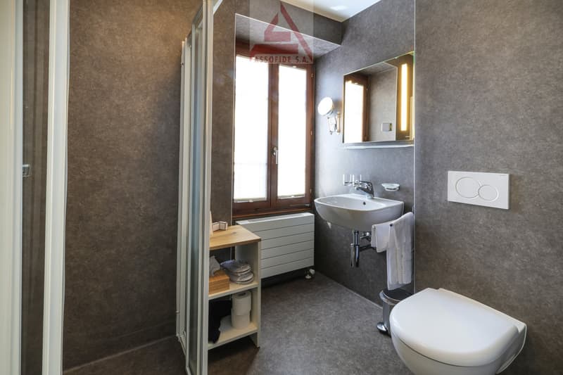 Bathroom with shower, sink, toilet, radiator, shelves, towels, and a window.