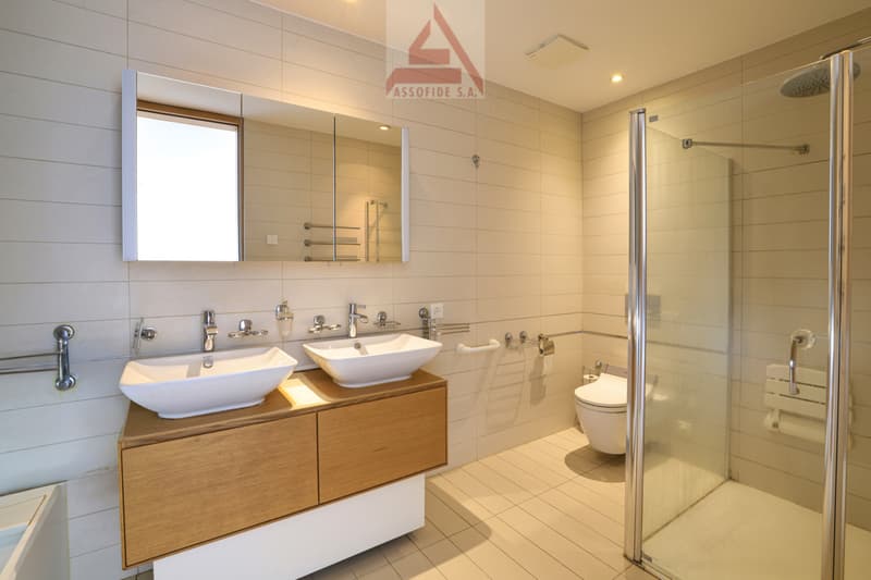 modern bathroom with double sink, shower, toilet, and wooden cabinet