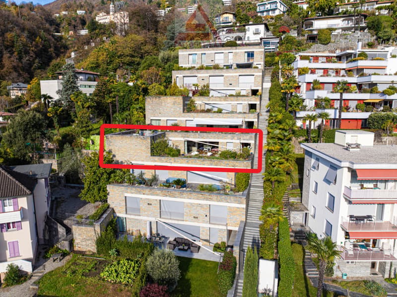 Aerial view of a multi-story house with a red outline, featuring a raised ground floor, multiple balconies, and a green rooftop terrace.