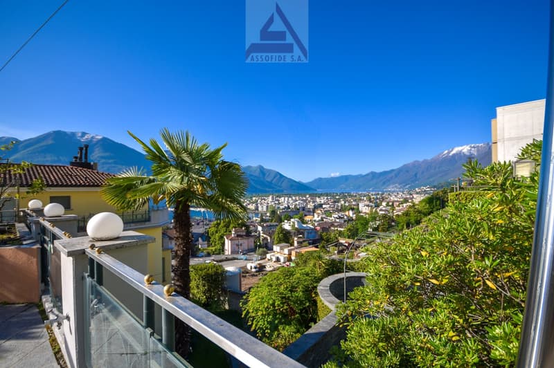 Balcony with glass railing, overlooking a town with mountains in the background