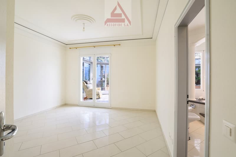 Empty room with white tiles, sliding glass doors leading to a balcony, white walls, and a ceiling with a logo.