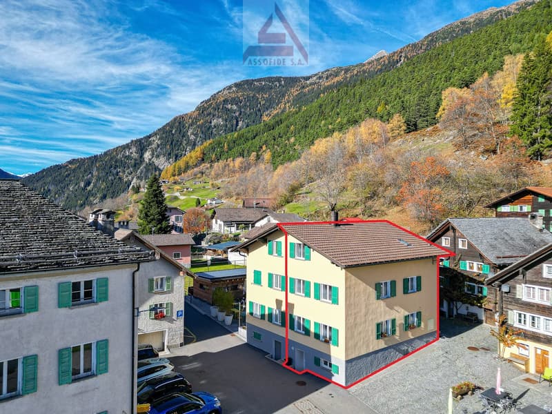 3-story house, yellow exterior, green shutters, brown roof, located in a mountainous area with a scenic view