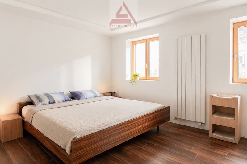 wooden bed, white bedding, wooden nightstands, white radiator, wooden shelves, wooden floor
