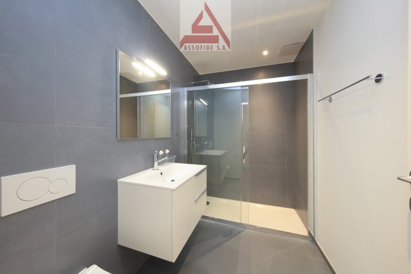 modern bathroom with white sink, mirror, glass shower enclosure, and gray tiles