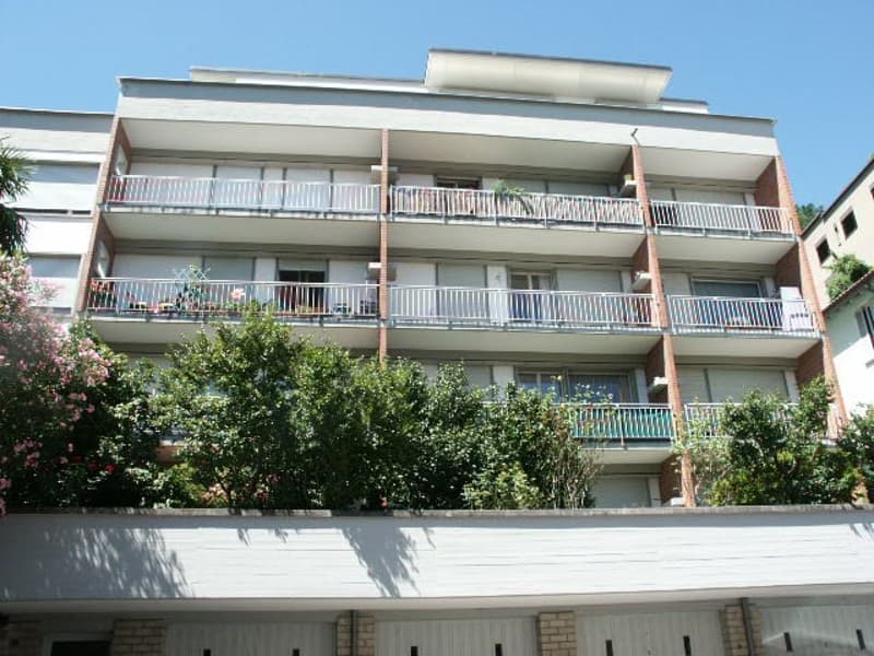 4-story apartment building with balconies on each floor, surrounded by trees and greenery
