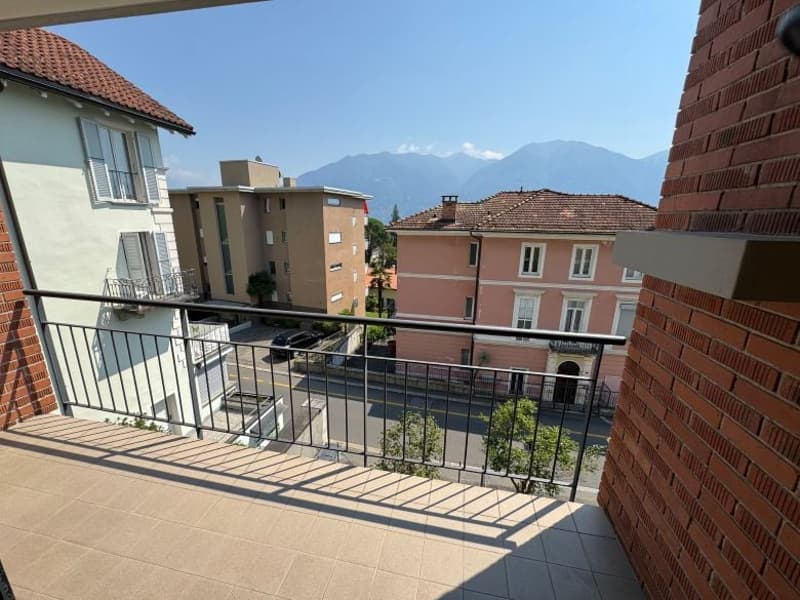Balcony with a metal railing, paved floor, with a city view and mountains in the background