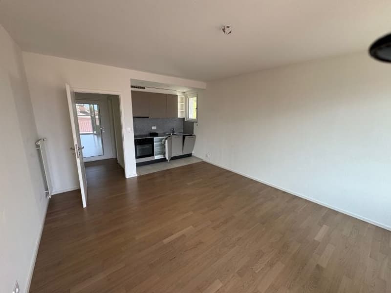 large room, open door, white walls, wooden floor, kitchen area, balcony, open view to the street