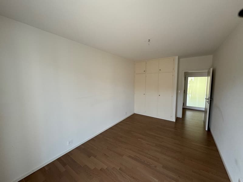 white walls, wooden floor, built-in cabinets, open door to another room