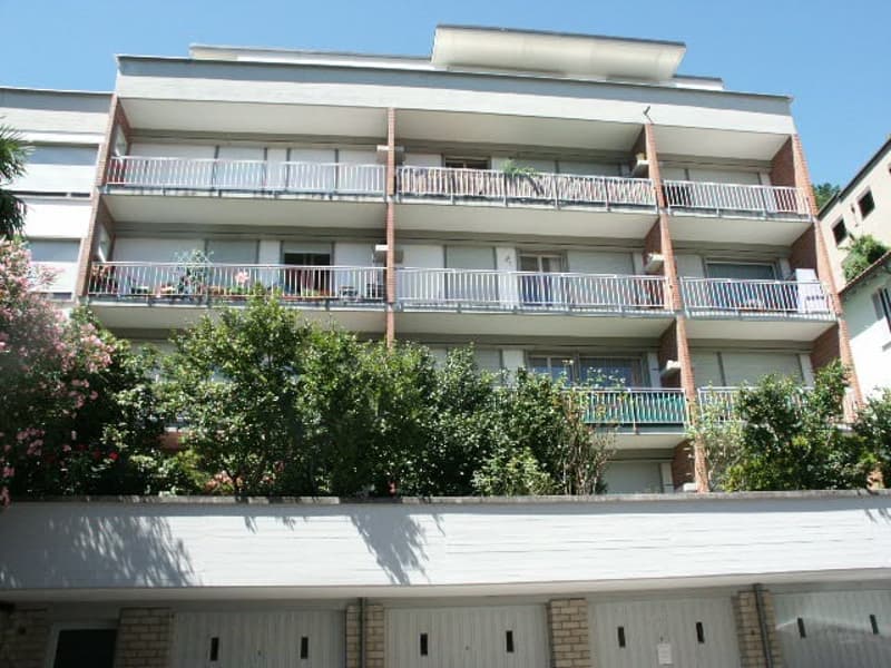 Multi-story apartment building with balconies on each floor, surrounded by trees and greenery