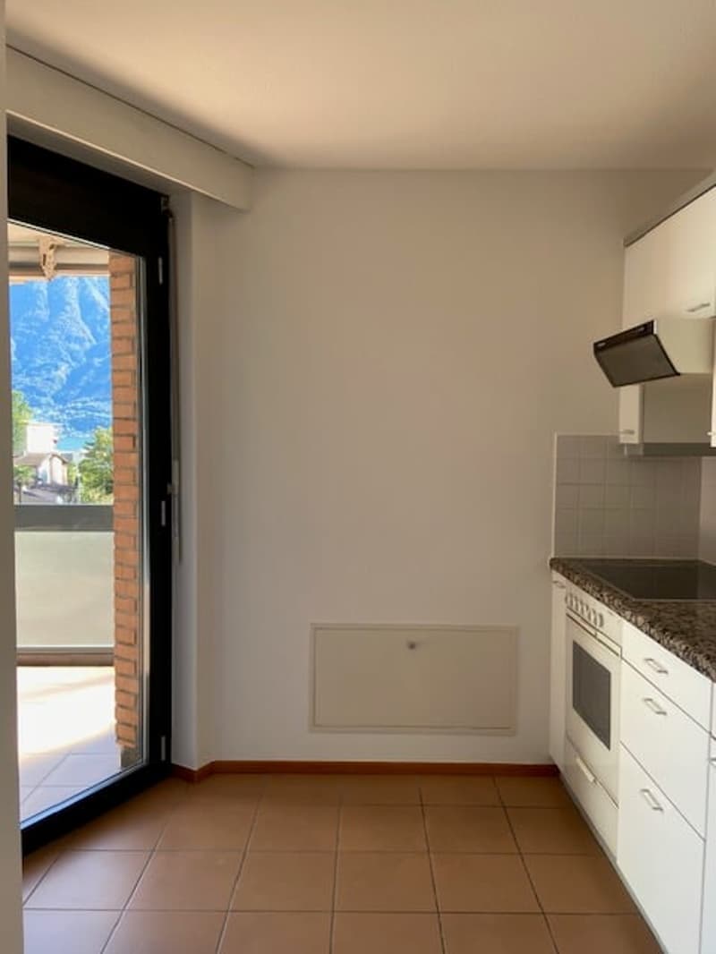 empty kitchen with modern design, brown tiled floor, sliding door leading to balcony, white cabinets, oven, granite countertop