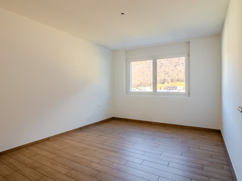Spacious bedroom with hardwood flooring, white walls, and large windows providing natural light and a view of the outdoor scenery.