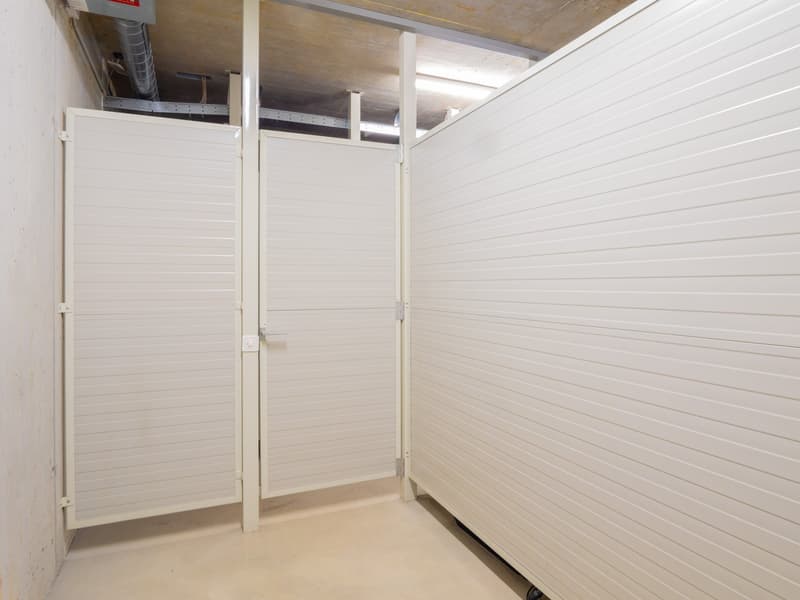 The image shows a small storage room with white paneled walls and shelving units. The room appears to be used for storage, with no other visible features.
