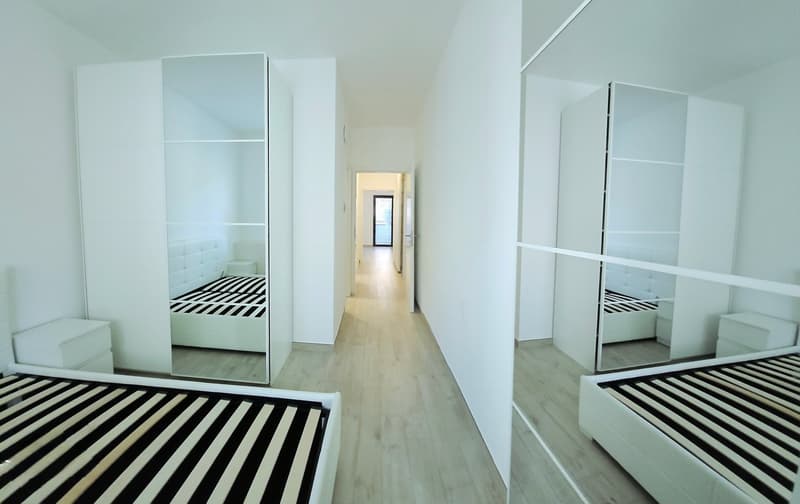 Bedroom, white walls, wooden floor, large mirrors, white beds, wardrobes, white nightstands.