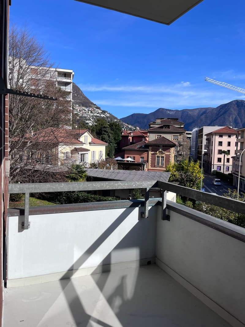Balcony with metal railing, white walls, white floor, view of the city and mountains
