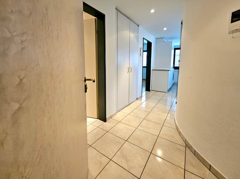 Empty hallway with white tiles, white walls, and a door leading to another room.