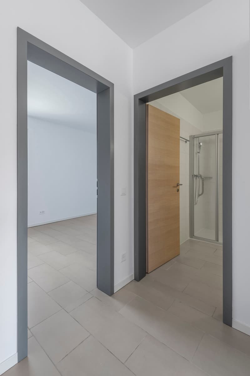 Empty room with tiled floor, white walls, wooden door, and a glass shower enclosure.
