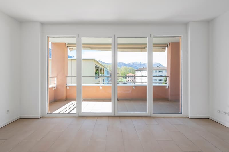 Empty room, modern design, large glass sliding doors leading to a balcony, tile floor, white walls, mountain view