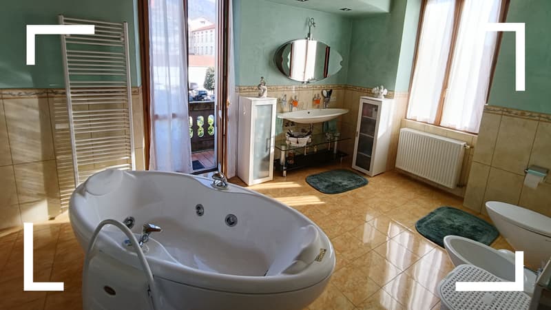 A bathroom with a bathtub, sink, mirror, radiator, green tiles, and a balcony