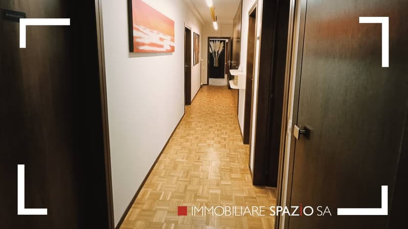 corridor with wooden flooring, white walls, doorways leading to rooms, paintings on the walls, open doors to the rooms