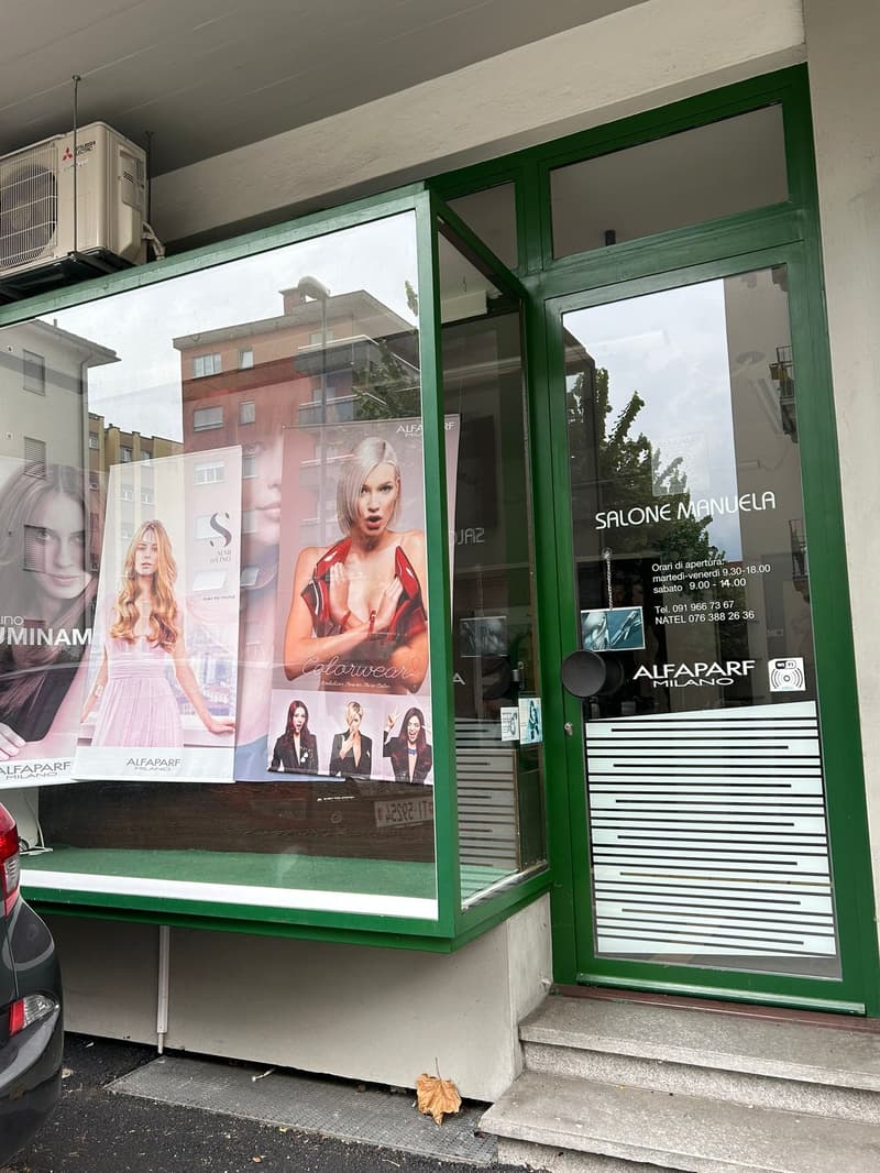 Storefront with a green frame, glass windows, advertisements featuring women, air conditioning unit on the ceiling, an open door, and a car parked on the side.