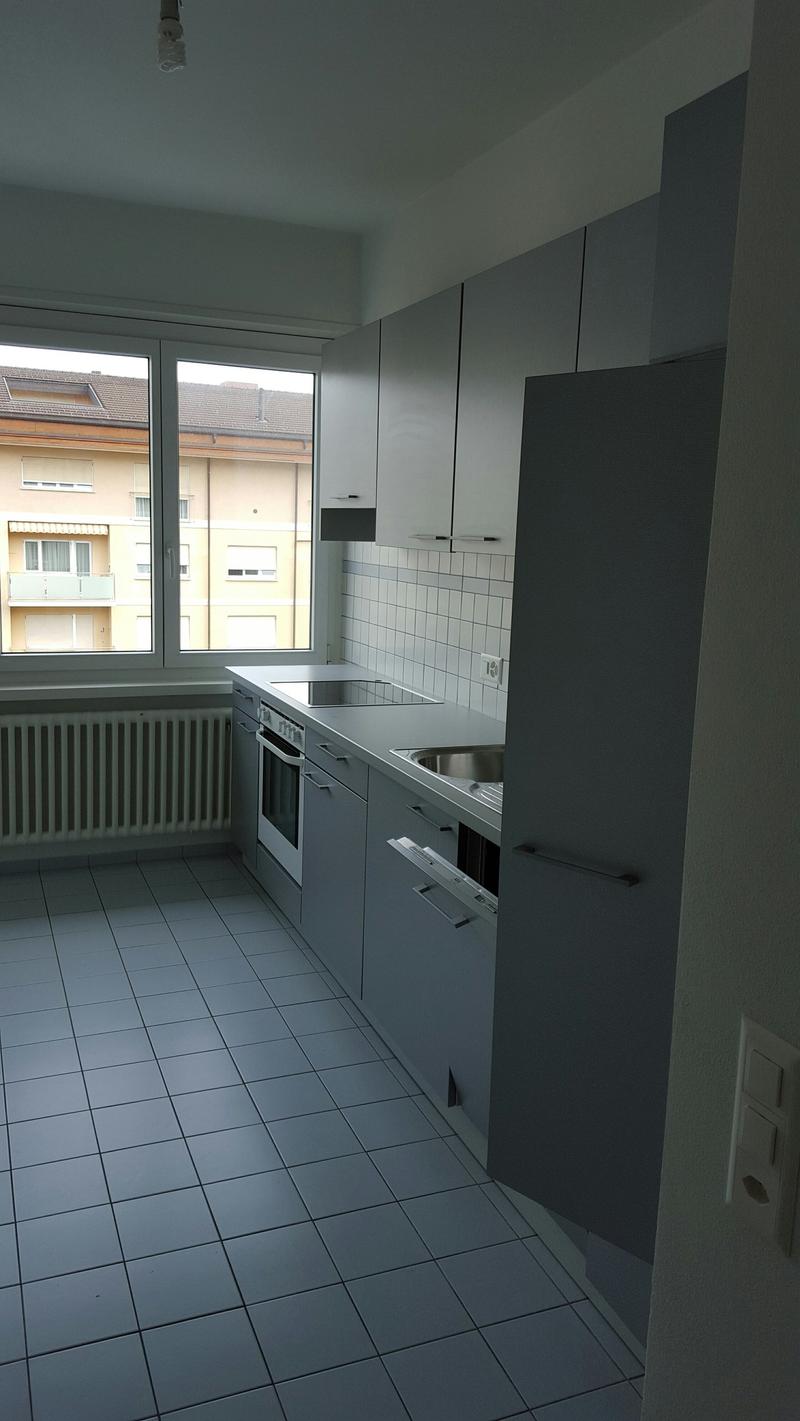 Empty kitchen with tile floor, windows, stainless steel sink, stove top, gas oven, radiator, cabinets and drawers.