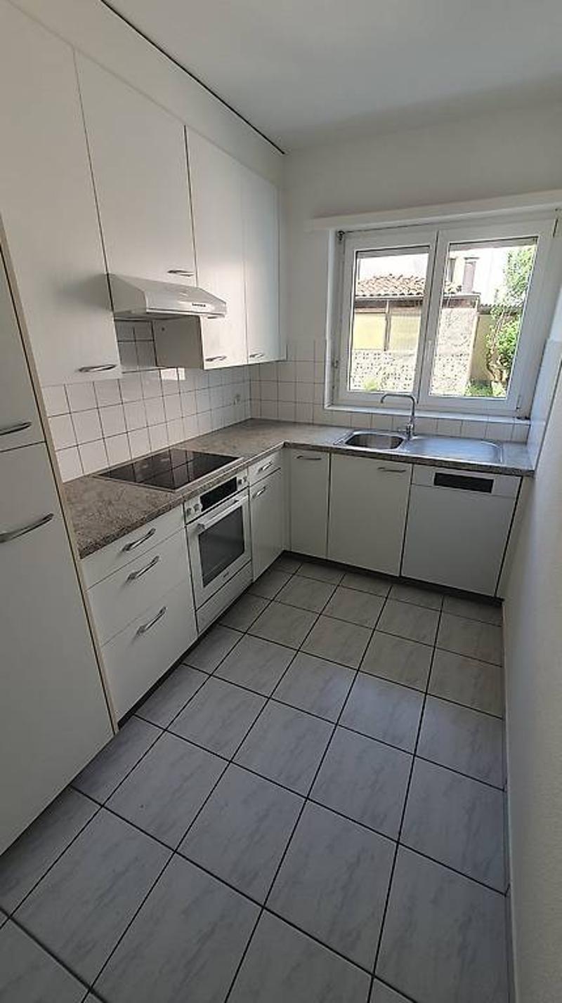 Compact L-shaped kitchen with white cabinets, tiled floor, and built-in appliances including a dishwasher