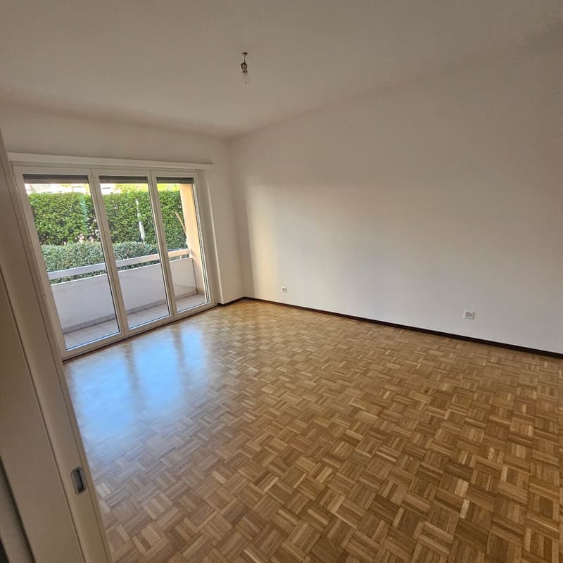 Spacious living room with large windows, hardwood parquet flooring, and access to a balcony or terrace.