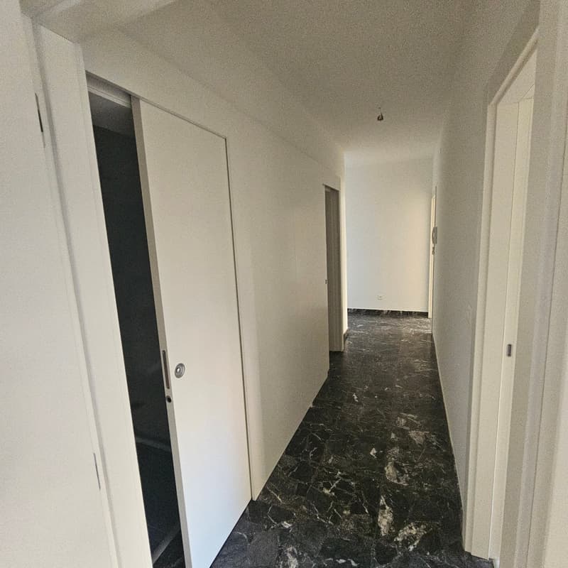 Long hallway with white walls, black marble flooring, and closed doors on either side.
