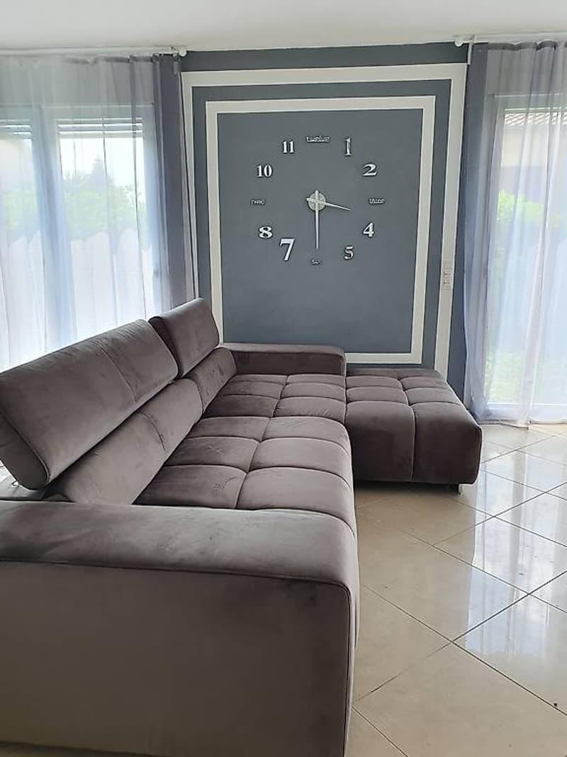 L-shaped sofa, gray walls, large clock, white curtains, tiled floor