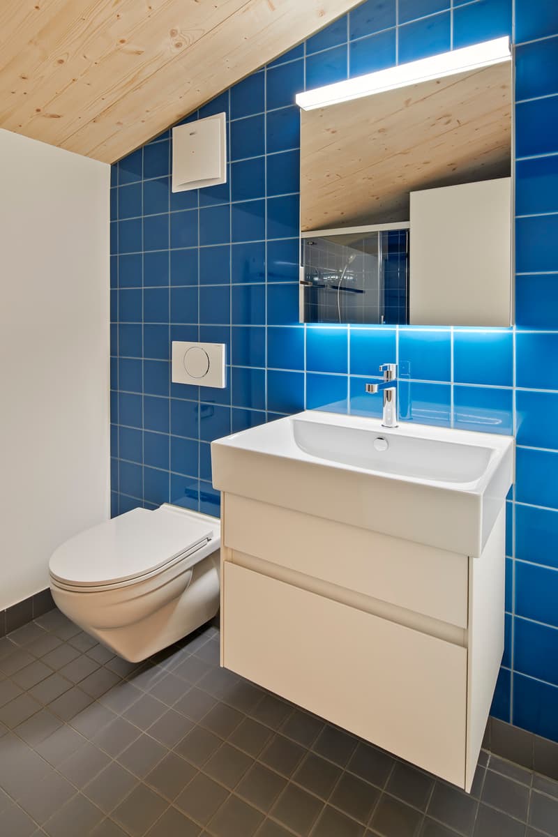 modern bathroom, blue tiles, white sink, toilet, shower area, under cabinet lighting, wooden ceiling