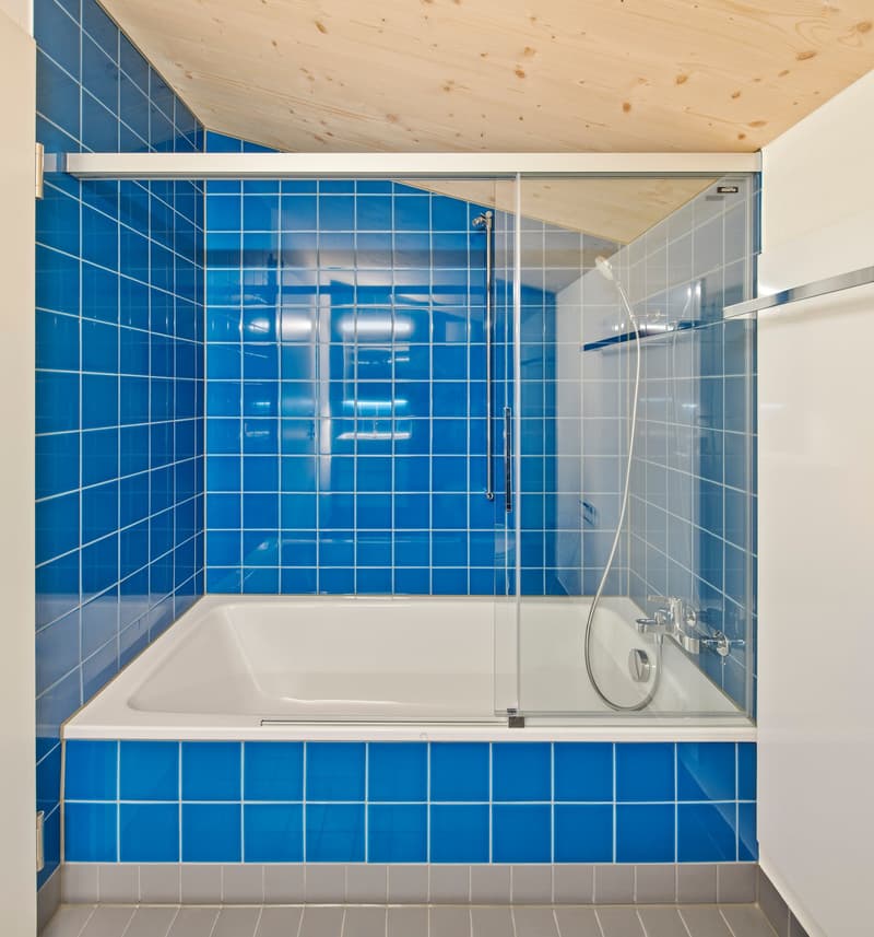 Bathroom with bathtub, shower, blue tiled walls, glass shower door, wooden ceiling