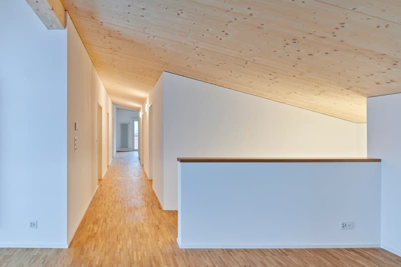 White walls, wooden floor, white ceiling with wooden beams, doorways, wall-mounted outlets